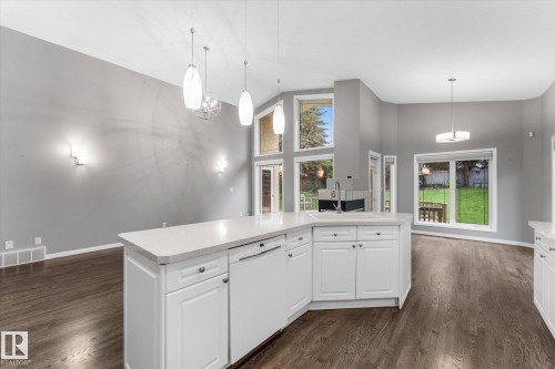 Open-concept living space featuring wood-finish flooring, white cabinetry, a kitchen island with a built-in sink, and large windows - 8 Osborne Close, St. Albert, AB - Indoor Photo Showing Kitchen