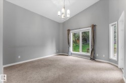 Vaulted ceiling featuring a chandelier, large windows, and neutral carpeting - 