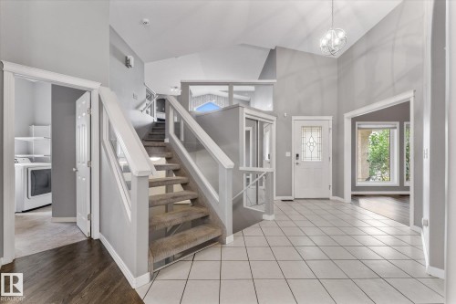 Vaulted ceiling, contemporary chandelier, white tile flooring, leaded glass front door, and a built-in laundry area - 8 Osborne Close, St. Albert, AB - Indoor Photo Showing Other Room