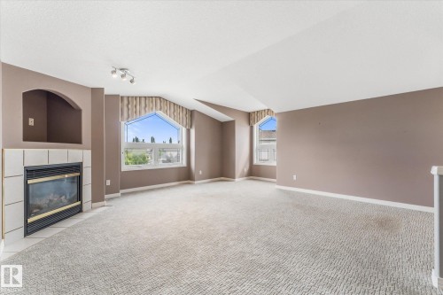 Built-in gas fireplace with tile surround, arched wall niche, vaulted ceilings, track lighting, and architectural windows - 8 Osborne Close, St. Albert, AB - Indoor With Fireplace