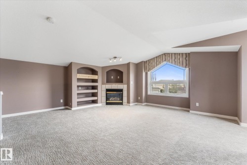 Integrated fireplace with stone surround, arched built-in shelving, track lighting, and a large arched window with valance - 8 Osborne Close, St. Albert, AB - Indoor With Fireplace