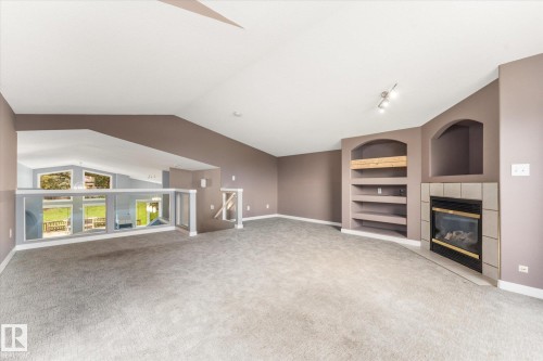 Carpeted interior with a gas fireplace, built-in shelving, vaulted ceilings, and an interior balcony with a glass railing - 8 Osborne Close, St. Albert, AB - Indoor Photo Showing Other Room With Fireplace