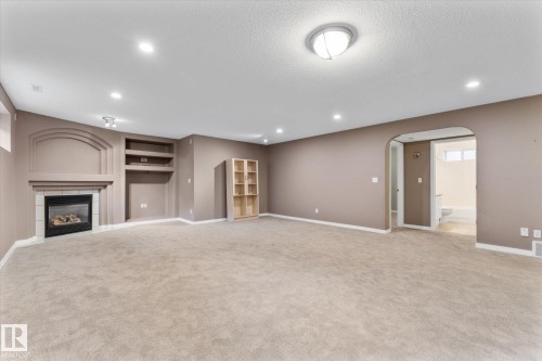 Spacious room featuring neutral carpeting, a built-in fireplace with a tiled surround, recessed lighting, and an arched entryway - 8 Osborne Close, St. Albert, AB - Indoor With Fireplace