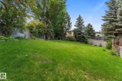 Expansive backyard featuring a lush lawn, mature trees, and privacy fencing - 