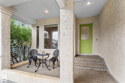 Covered porch area featuring textured stucco columns and walls, a lime green entry door with decorative glass, and a multi-paned window - 8 Osborne Close, St. Albert, AB - Outdoor With Exterior