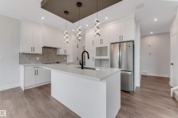 Contemporary kitchen featuring a large central island with a quartz countertop, white shaker-style cabinetry, stainless steel appliances, and wood-finish flooring - 