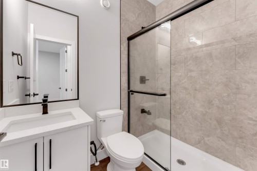 Bathroom featuring a modern vanity with integrated sink and quartz-finish countertop, black-framed mirror, and a glass-enclosed shower with subway tile surround and dark bronze hardware - 329 Balsam Link, Leduc, AB - Indoor Photo Showing Bathroom