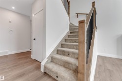 Carpeted staircase featuring integrated step lighting and a wood-finish railing with black metal spindles - 