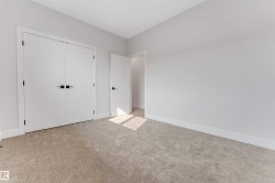 Neutral-toned carpeted room featuring a double-door closet with square black hardware and white baseboards - 