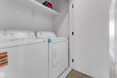 Dedicated laundry area featuring a white washer and dryer, white shelving, and a modern paneled door with dark hardware - 329 Balsam Link, Leduc, AB - Indoor Photo Showing Laundry Room