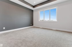 Room featuring a tray ceiling with recessed lighting, large window, gray accent wall, and light gray carpet flooring - 