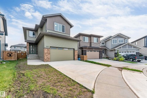 Contemporary two-story residence featuring a two-tone facade, attached front garage, concrete driveway, and a stone accent column - 329 Balsam Link, Leduc, AB - Outdoor With Facade