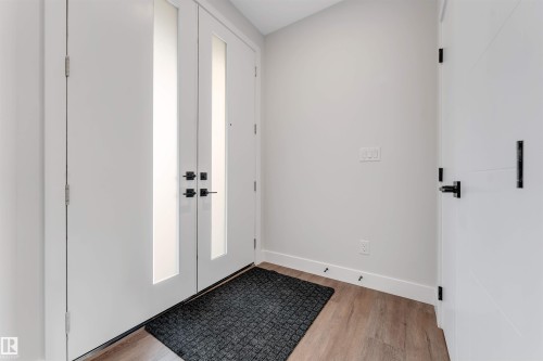 Double-door entry featuring vertical frosted glass panels and matte black hardware, complemented by light wood-finish flooring and white baseboards - 329 Balsam Link, Leduc, AB - Indoor Photo Showing Other Room