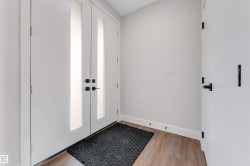 Double-door entry featuring vertical frosted glass panels and matte black hardware, complemented by light wood-finish flooring and white baseboards - 