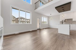 Two-story open concept living space featuring wood-finish flooring, a contemporary kitchen island with a built-in sink, and distinct pendant lighting fixtures - 