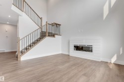 Contemporary living area featuring a modern linear fireplace with a white shiplap-style surround, two-story ceilings, wood-finish flooring, and a staircase with light wood newel posts and black metal spindles - 
