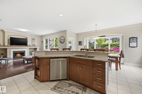 Kitchen island with granite countertop, integrated stainless steel dishwasher, and built-in shelving - 2416 Warry Place Sw, Edmonton, AB - Indoor Photo Showing Kitchen With Fireplace With Double Sink