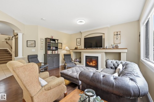 Living area with a gas fireplace, built-in media niche, wood-finish flooring, and natural light from large windows - 2416 Warry Place Sw, Edmonton, AB - Indoor Photo Showing Living Room With Fireplace