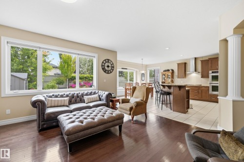 Hardwood-finish flooring throughout, large window with expansive glass panes, kitchen island with seating, stainless steel appliances, and a decorative column - 2416 Warry Place Sw, Edmonton, AB - Indoor Photo Showing Living Room