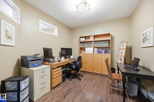 Wood-finish flooring, built-in shelving, two transom windows, and a flush mount ceiling light fixture - 2416 Warry Place Sw, Edmonton, AB - Indoor Photo Showing Office