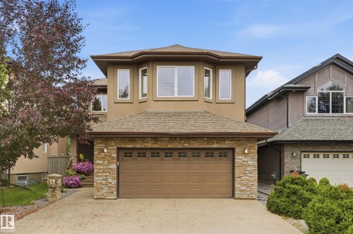Two-story home featuring a stone and stucco exterior with a covered entry, large picture windows, and a two-car garage door with paneled detailing - 2416 Warry Place Sw, Edmonton, AB - Outdoor