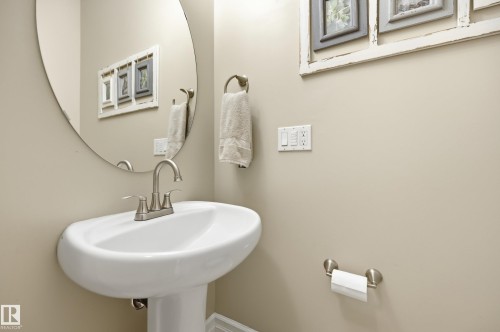 Pedestal sink with brushed nickel faucet, oval wall-mounted mirror, and neutral wall paint - 2416 Warry Place Sw, Edmonton, AB - Indoor Photo Showing Bathroom