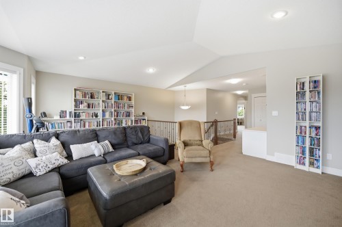 Spacious loft-style recreation room featuring soaring vaulted ceilings with recessed lighting, extensive built-in shelving throughout, neutral carpeting, and a railing-enclosed upper-level mezzanine accessible via interior staircase - 2416 Warry Place Sw, Edmonton, AB - Indoor Photo Showing Living Room