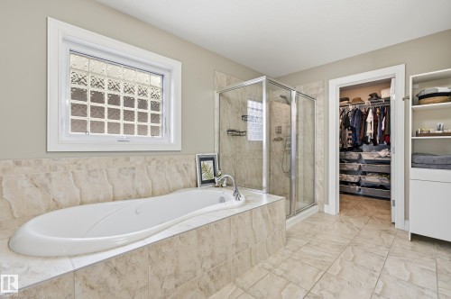 Built-in soaking tub with a tiled surround, glass block window, glass-enclosed shower, and tiled flooring - 2416 Warry Place Sw, Edmonton, AB - Indoor Photo Showing Bathroom