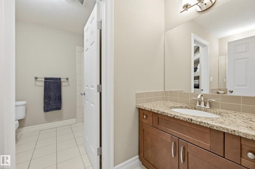 Warm-toned vanity with a granite-style countertop and an integrated sink, complemented by a large wall mirror and overhead lighting - 2416 Warry Place Sw, Edmonton, AB - Indoor Photo Showing Bathroom