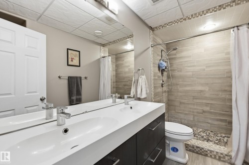 Dual vanity with integrated sinks, wood-finish flooring, tiled shower surround, pebble tile shower pan, and modern light fixtures - 2416 Warry Place Sw, Edmonton, AB - Indoor Photo Showing Bathroom