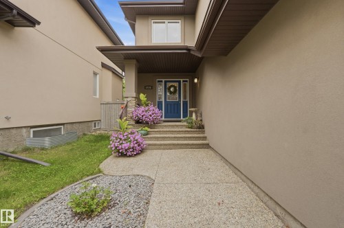 Stucco exterior with a blue entry door, concrete steps, and an exposed aggregate walkway - 2416 Warry Place Sw, Edmonton, AB - Outdoor With Deck Patio Veranda