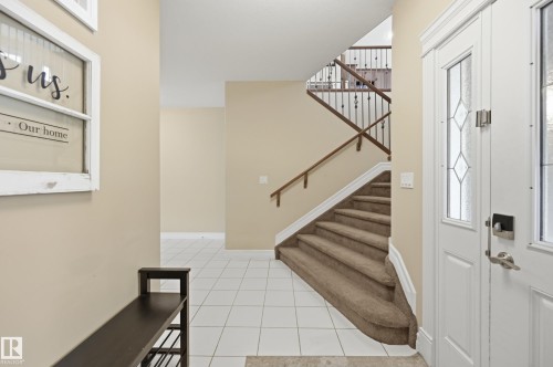 Foyer with white tile flooring, neutral wall tones, and a staircase featuring carpeted treads, wood handrails, and wrought iron balusters - 2416 Warry Place Sw, Edmonton, AB - Indoor Photo Showing Other Room