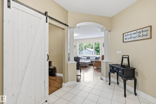 Entryway featuring a white sliding barn door with black hardware, tile flooring, and an arched doorway opening to the main living spaces - 2416 Warry Place Sw, Edmonton, AB - Indoor Photo Showing Other Room
