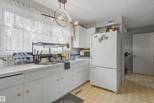 Galley kitchen featuring white cabinetry, a double basin sink, a large window, and patterned flooring - 5724 143 Avenue Nw, Edmonton, AB - Indoor Photo Showing Kitchen With Double Sink