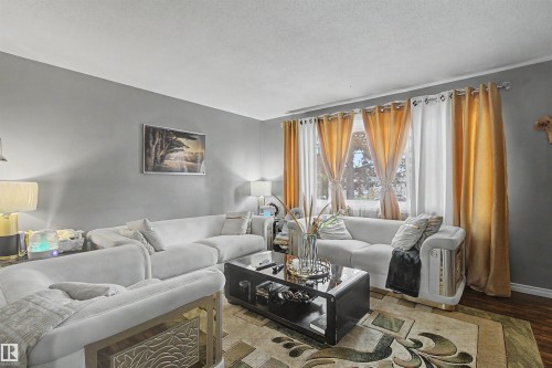 Room featuring neutral wall tones, multiple windows with rod-pocket curtains, and wood-finish flooring - 5724 143 Avenue Nw, Edmonton, AB - Indoor Photo Showing Living Room