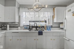 White cabinetry with gold-tone hardware, a double basin sink with a matte black faucet, and a contemporary linear chandelier with globe lights - 