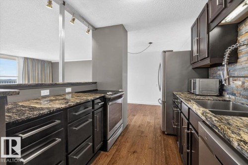 Kitchen featuring wood-finish flooring, dark cabinetry, stone countertops, and a stone-tiled backsplash - #506 12121 Jasper Av Nw, Edmonton, AB - Indoor Photo Showing Kitchen With Double Sink With Upgraded Kitchen