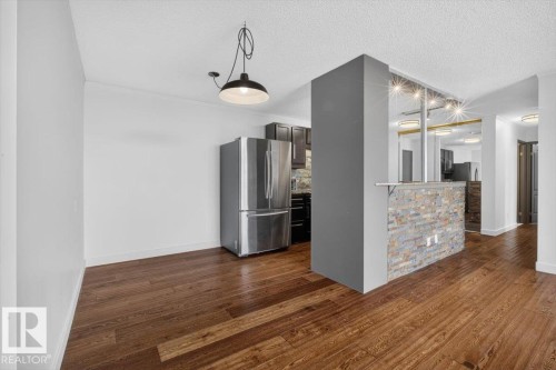 Wood-finish flooring throughout, stainless steel refrigerator, dark wood cabinetry, and a stone-clad breakfast bar with integrated lighting - #506 12121 Jasper Av Nw, Edmonton, AB - Indoor