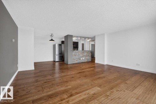 Open concept living area featuring wood-finish flooring, a stone-clad breakfast bar, and stainless steel appliances - #506 12121 Jasper Av Nw, Edmonton, AB - Indoor Photo Showing Other Room