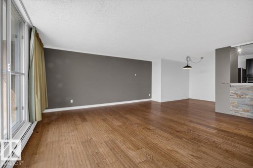 Expansive room featuring wood-finish flooring, a full-height window, crown molding, and a stone-clad half-wall - #506 12121 Jasper Av Nw, Edmonton, AB - Indoor Photo Showing Other Room