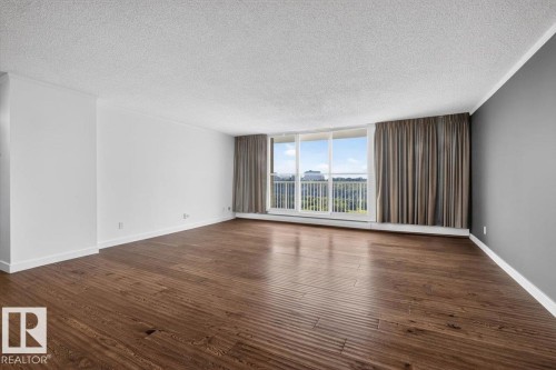 Spacious room featuring wood-finish flooring, a full-height window, and a balcony with metal railing - #506 12121 Jasper Av Nw, Edmonton, AB - Indoor Photo Showing Other Room
