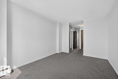 Spacious room featuring neutral grey carpeting, white painted walls, a mirrored closet door, and a flush mount ceiling light in the hallway - #506 12121 Jasper Av Nw, Edmonton, AB - Indoor Photo Showing Other Room