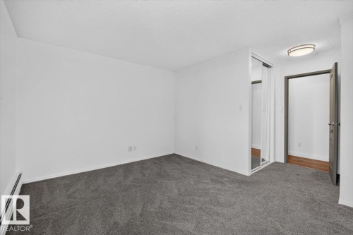 Spacious room featuring neutral carpeting, a mirrored closet, and a contemporary ceiling light fixture - #506 12121 Jasper Av Nw, Edmonton, AB - Indoor Photo Showing Other Room