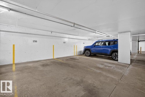 Concrete parking area featuring a painted concrete floor, bright overhead lighting, and numbered wall spaces - #506 12121 Jasper Av Nw, Edmonton, AB - Indoor Photo Showing Garage