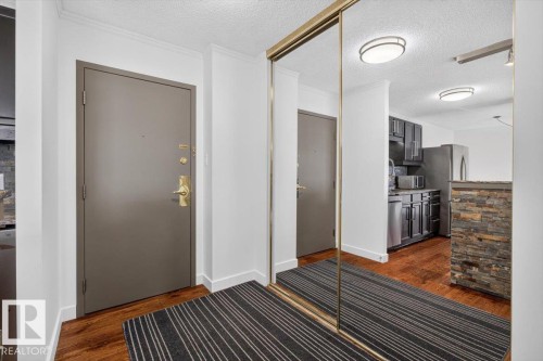 Full-height mirrored closet doors, wood-finish flooring, and a stone-clad half-wall - #506 12121 Jasper Av Nw, Edmonton, AB - Indoor