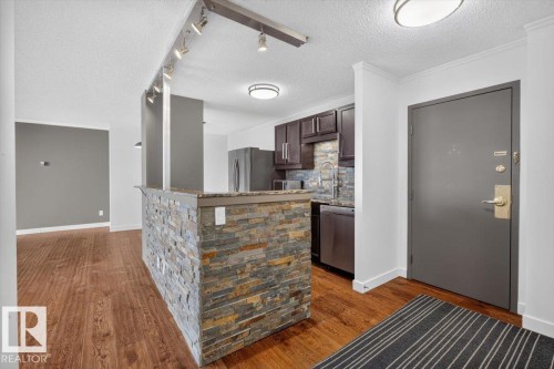 Hardwood-finish flooring, stone-clad breakfast bar, dark wood cabinetry, stainless steel appliances, and track lighting - #506 12121 Jasper Av Nw, Edmonton, AB - Indoor Photo Showing Kitchen