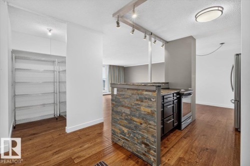 Kitchen area featuring a stacked stone island, dark wood-finish flooring, stainless steel appliances, and track lighting - #506 12121 Jasper Av Nw, Edmonton, AB - Indoor Photo Showing Kitchen