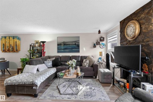 Living area featuring wood-finish flooring, a stacked stone accent wall, and crown molding - 17127 109 Street Nw, Edmonton, AB - Indoor Photo Showing Living Room