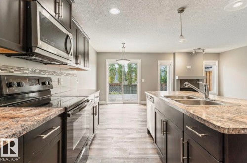 Modern kitchen featuring dark wood-finish cabinetry, stainless steel appliances, a tile backsplash, and a double basin sink - 79 Catalina Crest, Fort Saskatchewan, AB - Indoor Photo Showing Kitchen With Double Sink With Upgraded Kitchen