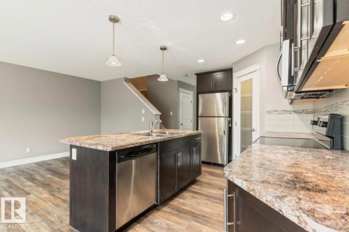 Kitchen featuring wood-finish flooring, dark cabinetry, stainless steel appliances, a kitchen island with seating, and pendant lighting - 79 Catalina Crest, Fort Saskatchewan, AB - Indoor Photo Showing Kitchen With Double Sink With Upgraded Kitchen